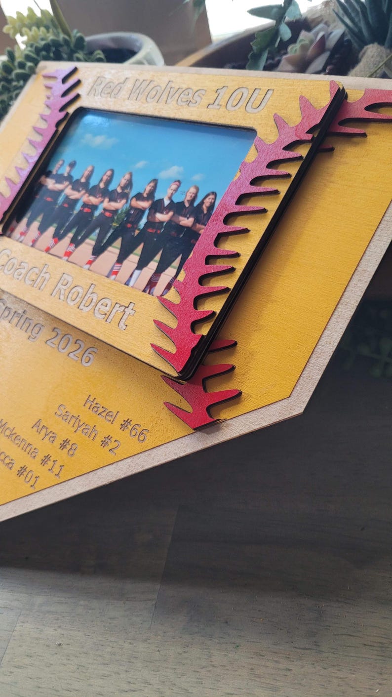 May include: A wooden photo frame with a team photo. The frame is yellow with red accents and the text "Red Wolves 10U", "Coach Robert", and "Spring 2026". Names and numbers are also engraved on the frame.