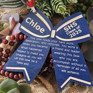 May include: A blue wooden bow with the text "Chloe" and "SHS Class of 2025" on it. The bow has a message about hard work, dedication, and victories.