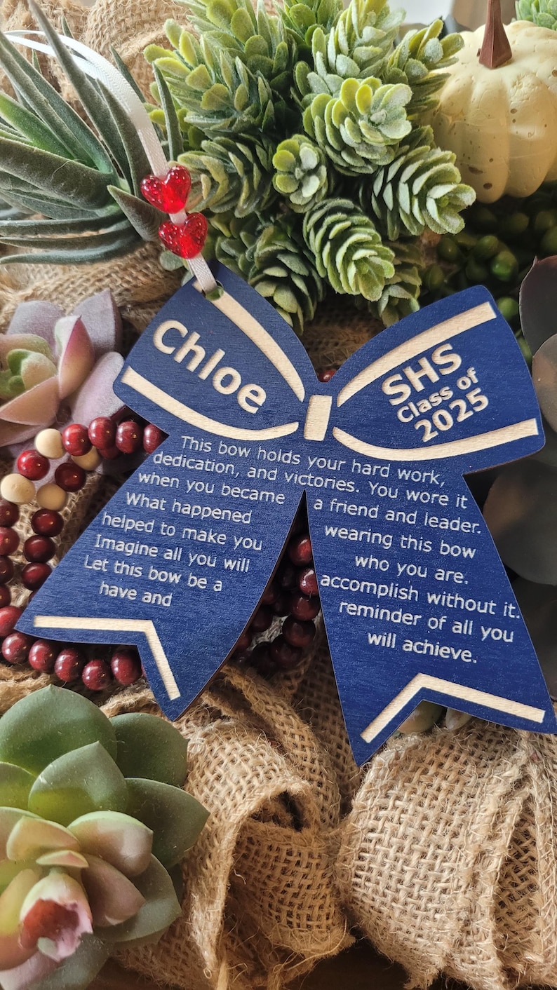 May include: A blue wooden bow with the text "Chloe" and "SHS Class of 2025" on it. The bow has a message about hard work, dedication, and victories.