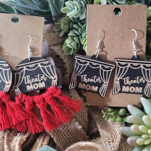 May include: Two pairs of black wooden earrings with red tassels. The earrings feature a black curtain design with the text "Theater Mom" on each earring.