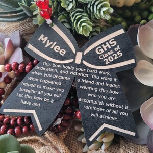 May include: A black wooden bow with the name "Mylee" and the text "GHS Class of 2025" on it. The bow has a message about hard work, dedication, and victories.