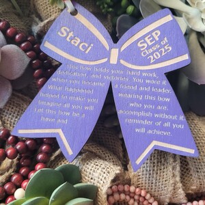 May include: Purple wooden bow with the text "Staci" and "SEP Class of 2025" on it. The bow has a message about hard work, dedication, and victories.