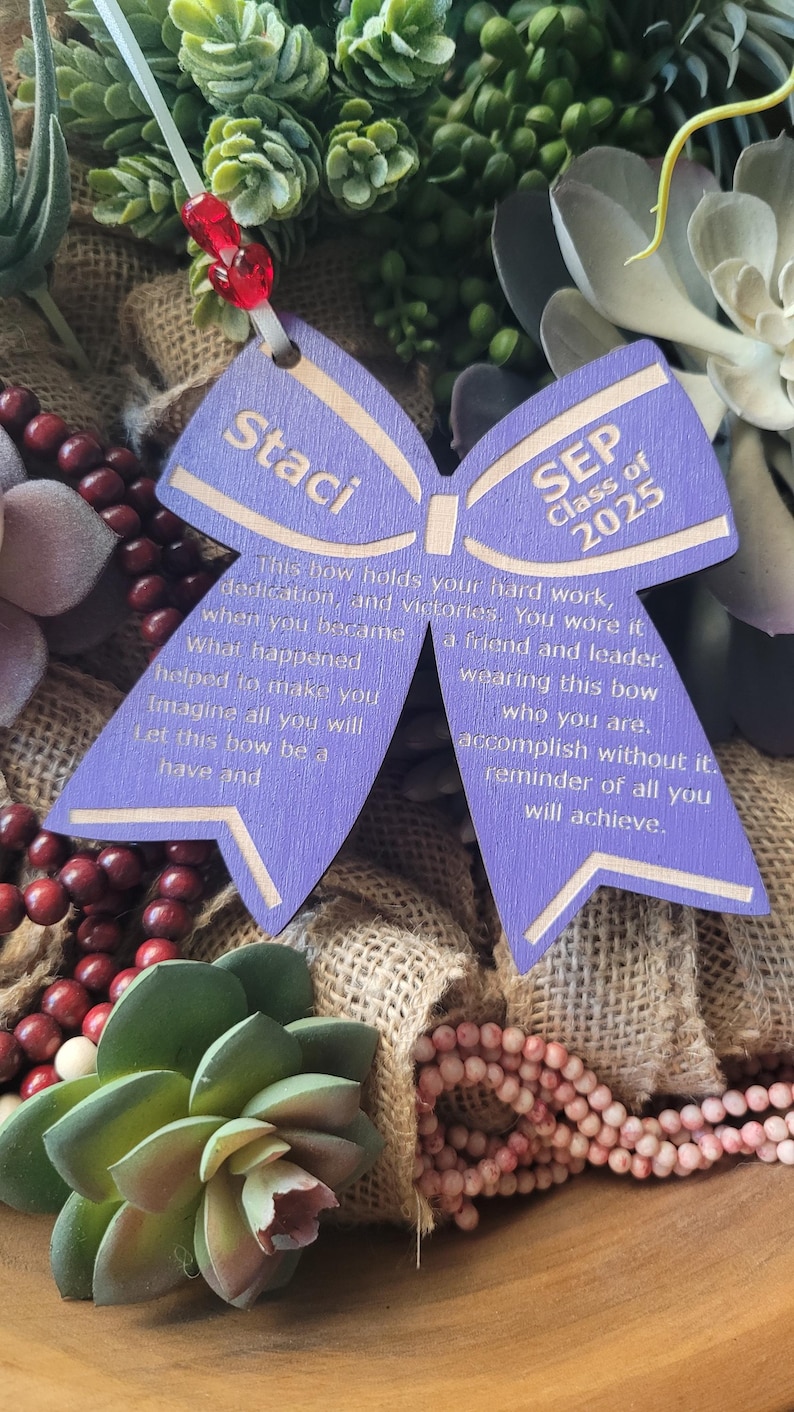 May include: Purple wooden bow with the text "Staci" and "SEP Class of 2025" on it. The bow has a message about hard work, dedication, and victories.