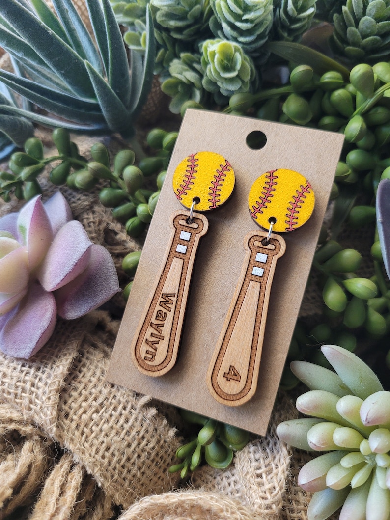 Puede incluir: Un par de pendientes colgantes con un dije de s&oacute;ftbol amarillo unido a un dije de bate de b&eacute;isbol de madera clara. Un bate est&aacute; grabado con el nombre Waylyn y el otro bate est&aacute; grabado con el n&uacute;mero 4. Los pendientes se presentan en una tarjeta.