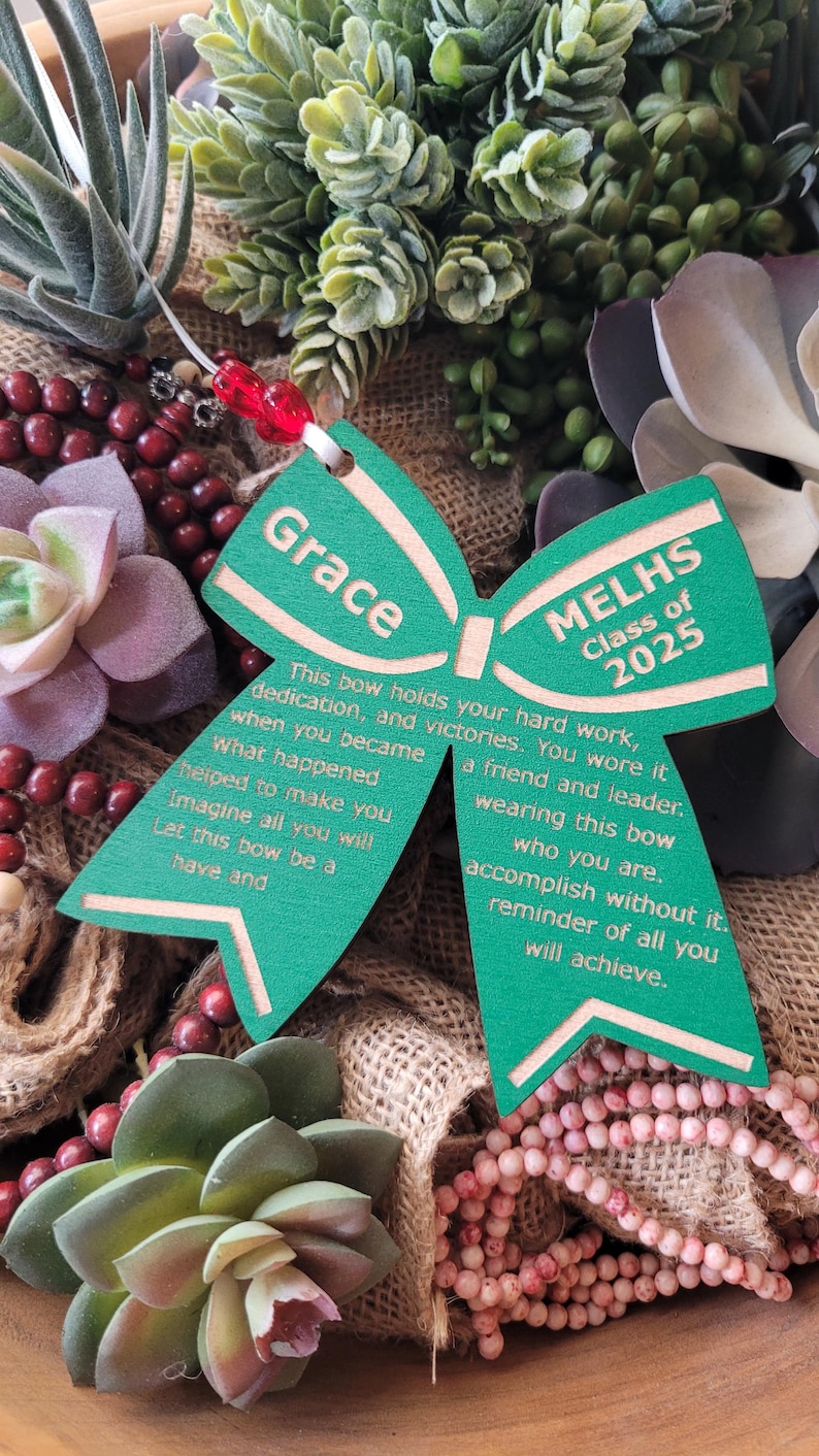 May include: Green wooden bow with the text "Grace" and "MELHS Class of 2025" on it. The bow has a message about hard work, dedication, and victories.