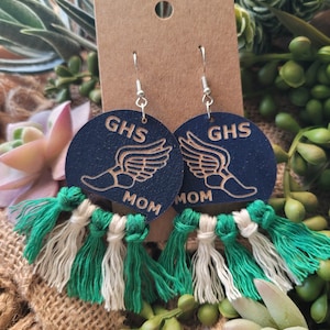 May include: A pair of blue and white wooden earrings with green tassels. The earrings feature a winged foot and the text "GHS MOM".