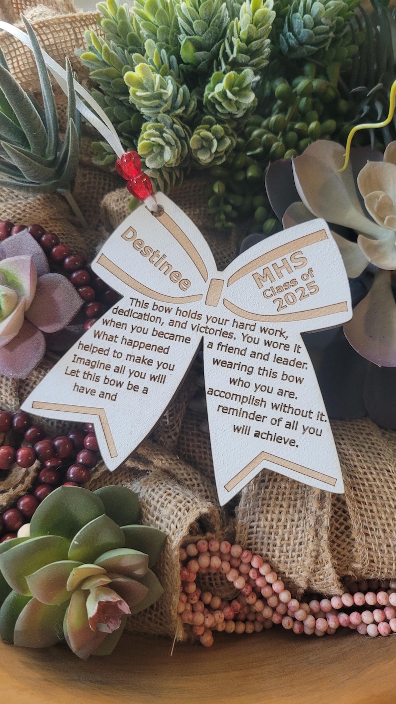 May include: A wooden bow with the text "Destinee" and "MHS Class of 2025" on it. The bow has a message about hard work, dedication, and victories.