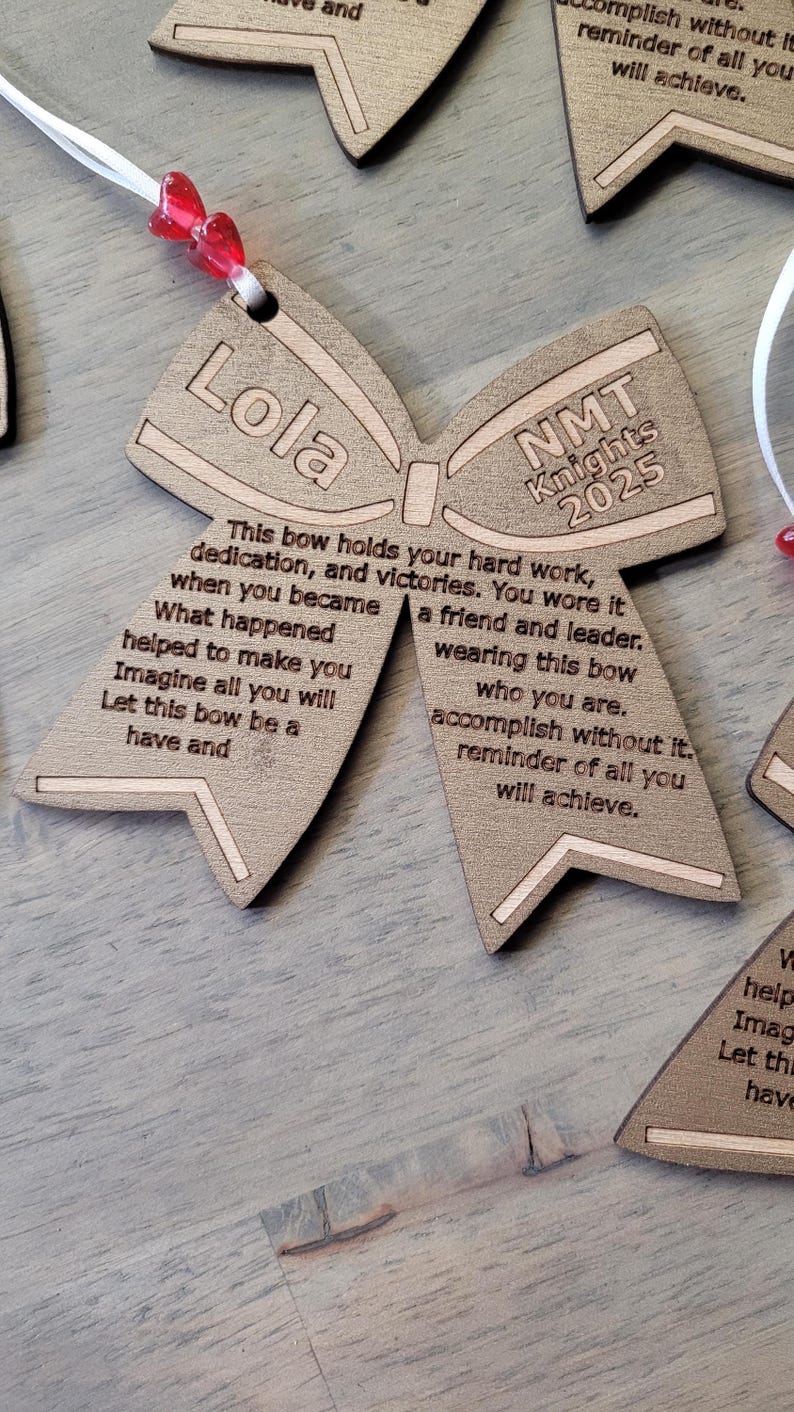 May include: A wooden bow tie ornament with the text "Lola" on one side and "NMT Knights 2025" on the other side. The ornament has a message about hard work, dedication, and victories.