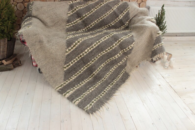 May include: A gray and white striped wool throw blanket with fringe edges. The blanket is draped over a couch.