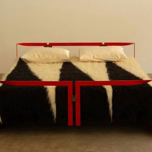 Puede incluir: Una moderna estructura de cama en rojo brillante con una manta estampada en blanco y negro. Dos almohadas color crema descansan sobre la cama. La estructura de la cama tiene un diseño minimalista.