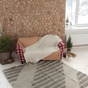 May include: A cozy living room with a plaid couch, a white throw blanket, and a gray and white striped rug. The wall is made of wood rounds and there are small potted trees in the room.