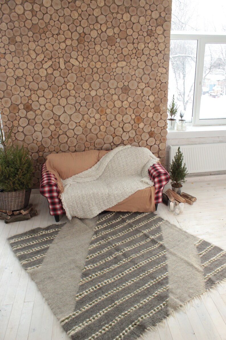 May include: A cozy living room with a plaid couch, a white throw blanket, and a gray and white striped rug. The wall is made of wood rounds and there are small potted trees in the room.