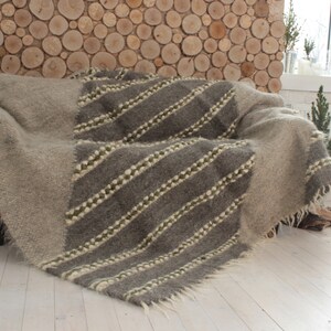 May include: A gray and white woven throw blanket with a diagonal pattern of stripes. The blanket is draped over a couch with a wooden wall behind it.