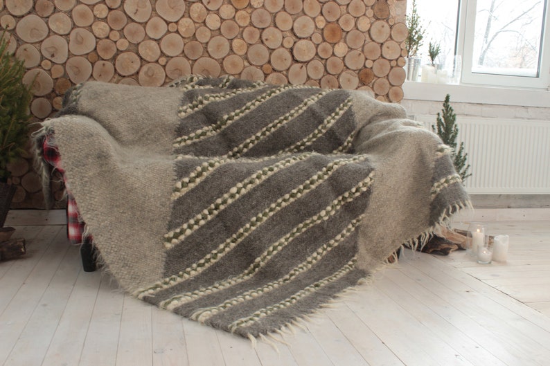 May include: A gray and white woven throw blanket with a diagonal pattern of stripes. The blanket is draped over a couch with a wooden wall behind it.