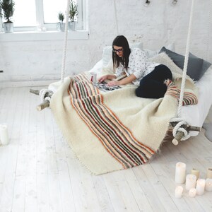 May include: A woman sits on a white bed with a striped blanket, reading a book. There are candles on the floor.