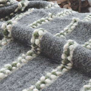 May include: A gray knitted throw blanket with white and green pom-poms along the edges.