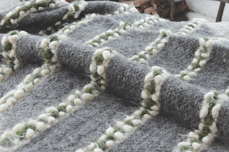 May include: A gray knitted throw blanket with white and green pom-poms along the edges.
