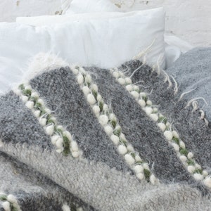 May include: A gray and white woven throw blanket with green accents. The blanket has a textured, fuzzy surface and is folded on a bed.