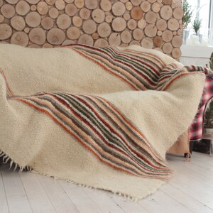 May include: A white throw blanket with multi-colored stripes in shades of brown, orange, green, and red. The blanket is draped over a red and white plaid couch.