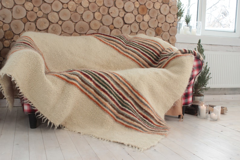 May include: A white throw blanket with multi-colored stripes in shades of brown, orange, green, and red. The blanket is draped over a red and white plaid couch.