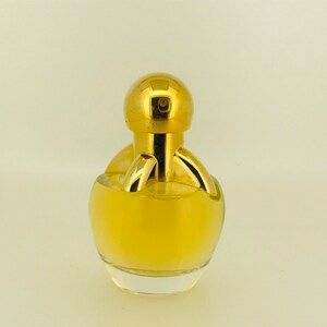 May include: A gold perfume bottle with a round, clear glass body and a gold cap. The bottle has a unique design with a gold ring around the neck and a gold knob on top.