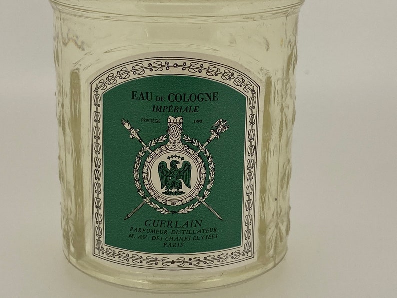 May include: A clear glass bottle with a green and white label that reads "EAU DE COLOGNE IMP&Eacute;RIALE" and "GUERLAIN PARFUMEUR DISTILLATEUR 6. AV. DES CHAMPS-ELYSEES PARIS".