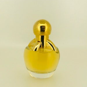 May include: A gold perfume bottle with a round, clear glass body and a gold cap. The bottle has a unique design with a gold ring around the neck and a gold knob on top.
