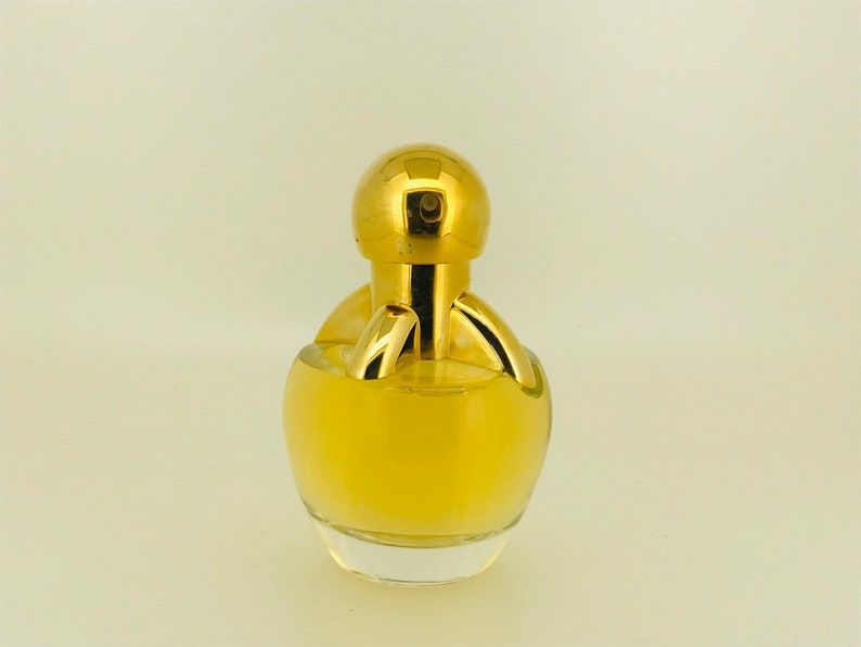 May include: A gold perfume bottle with a round, clear glass body and a gold cap. The bottle has a unique design with a gold ring around the neck and a gold knob on top.