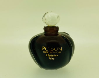 May include: A dark brown glass bottle of Poison perfume by Christian Dior. The bottle has a unique, curvy shape and a clear glass stopper. The label reads "Poison Esprit de Parfum Christian Dior Paris".