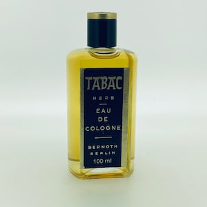 May include: A clear glass bottle of Tabac Herb Eau de Cologne, with a black cap and gold label. The label reads "Tabac Herb Eau de Cologne" and "Bernoth Berlin 100 ml".