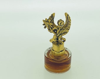 以下が含まれることがあります： 花を持った羽根つきの天使の像が付いた金色のボトルストッパー。ストッパーは透明なガラスの台座の上にあり、中には茶色の液体が入っています。