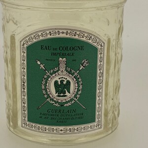 May include: A clear glass bottle with a green and white label that reads "Eau de Cologne Imp&eacute;riale" and "Guerlain Parfumeur Distillateur 6. Av. des Champs-&Eacute;lys&eacute;es Paris".