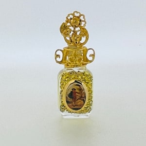 May include: A small, clear glass bottle with a gold-colored stopper and a gold-colored frame around a picture of a person. The bottle is filled with gold glitter.