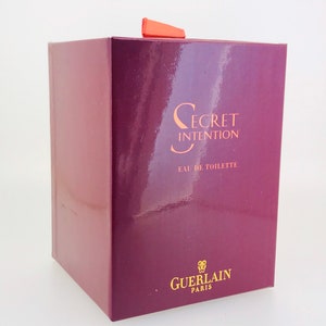 May include: A burgundy box with a gold label that reads "Secret Intention Eau de Toilette Guerlain Paris".