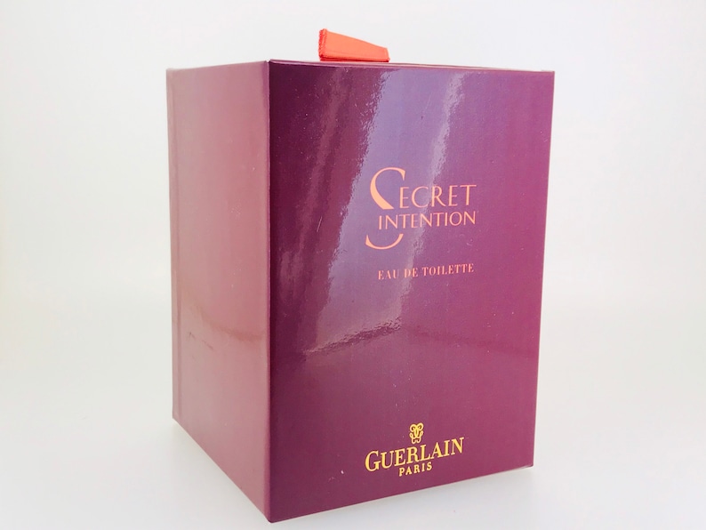 May include: A burgundy box with a gold label that reads "Secret Intention Eau de Toilette Guerlain Paris".
