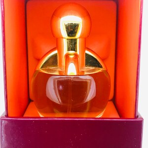 May include: A gold and clear glass perfume bottle with a round, bulbous top. The bottle is sitting inside a burgundy box with an orange interior.