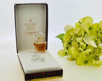 May include: A small bottle of Guerlain L'Heure Bleue perfume in a red and gold box. The bottle is clear glass with a gold cap and a gold label that says "L'Heure Bleue Parfum Guerlain Paris".