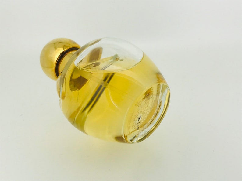 May include: A clear glass bottle with a gold cap and a yellow liquid inside. The bottle is lying on its side and the bottom of the bottle is visible. The bottom of the bottle has the word "DELVYN" printed on it.