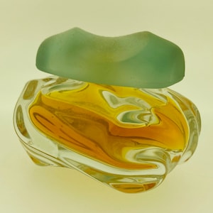 May include: A clear glass bottle containing a yellow liquid. The bottle has a distinctive, wavy design and a frosted glass lid.