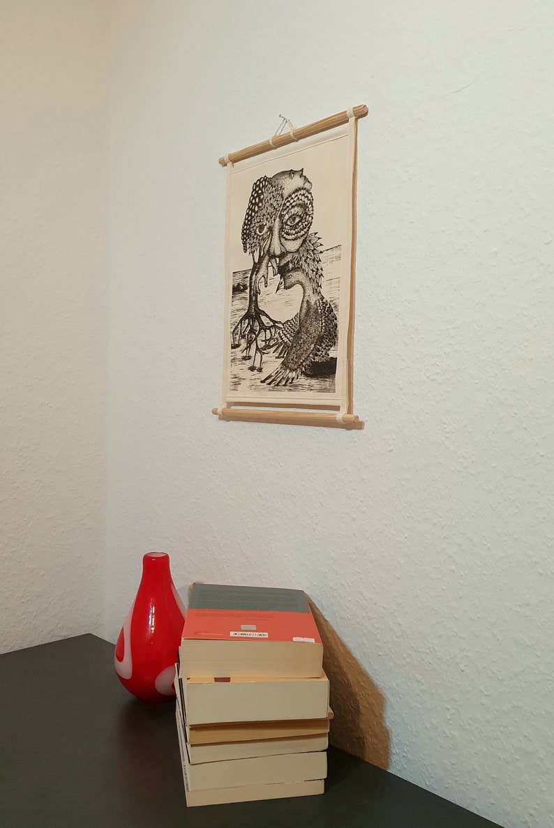 May include: A black and white illustration of a creature with a human-like face and a tree-like body. The illustration is printed on a canvas and framed with a wooden dowel. The canvas is hanging on a white wall.