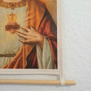 May include: A vintage religious print of Jesus Christ with a crown of thorns and a bleeding heart. The print is framed with a white border and a wooden dowel rod.