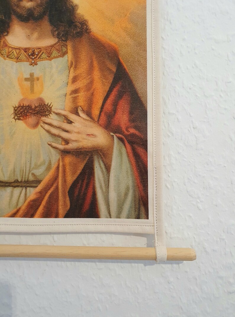 May include: A vintage religious print of Jesus Christ with a crown of thorns and a bleeding heart. The print is framed with a white border and a wooden dowel rod.