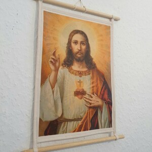 May include: A canvas print of a religious image depicting Jesus Christ with a crown of thorns and a bleeding heart. The image is framed with a wooden dowel rod.