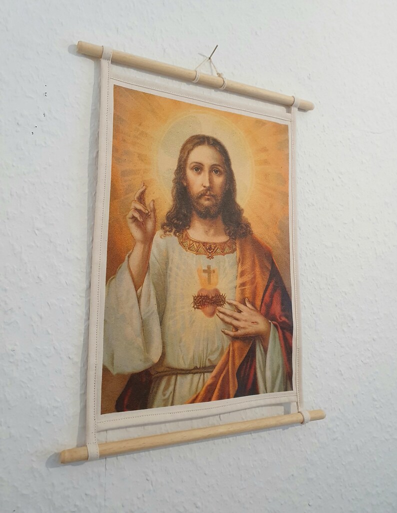 May include: A canvas print of a religious image depicting Jesus Christ with a crown of thorns and a bleeding heart. The image is framed with a wooden dowel rod.