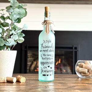 Clear recycled winefrosted with spray paint. Black vinyl words It's the friends we meet along the way that help us appreciate the Journey. Includes batteryoperated fairy lights attached to plastic cork with on/off switch. Topped off with twine and your choice of ribbons.