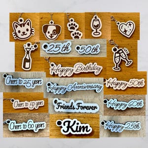 May include: A selection of wooden keyrings with diverse designs. Includes a cat, dog, paw prints, wine glass, heart, champagne bottle, and phrases such as "Happy Birthday" and "Friends Forever." Some keyrings feature numbers.