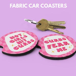 May include: Fabric car coasters with pink and white checkered patterns and the phrases "HOT GIRLS HIT CURBS" and "CURBS FEAR ME" in red text. A set of keys rests above the coasters on a purple background.