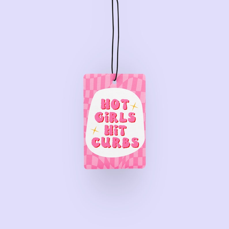 May include: Pink car air freshener with a white oval containing the text "HOT GIRLS HIT CURBS" in pink bubble letters. The background is a pink and white checkered pattern.