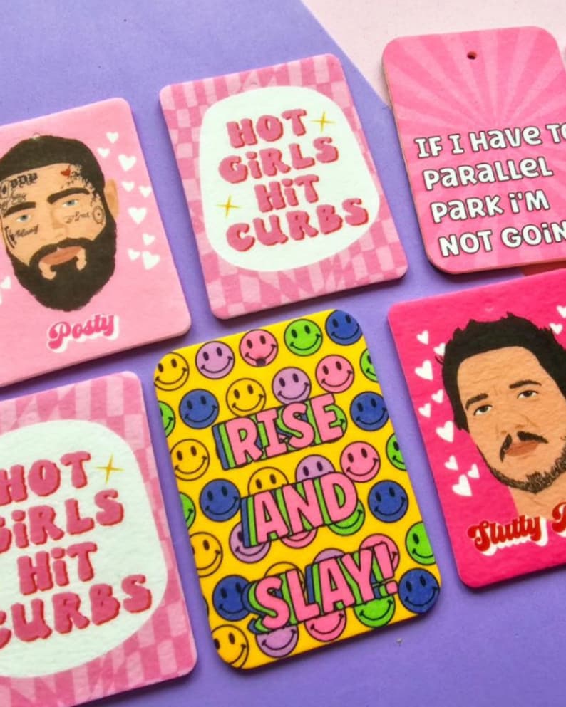 May include: Six pink and yellow car air fresheners with various designs and text. The designs include a smiley face pattern, a pink and white checkered pattern, and a pink heart pattern. The text includes "Hot Girls Hit Curbs", "Rise and Slay", "If I Have To Parallel Park I'm Not Going", and "Slutty 9".