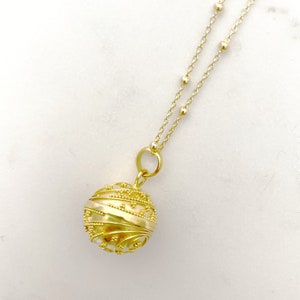 May include: A gold necklace with a delicate chain and a round, ornate pendant. The pendant has a textured, swirling design.